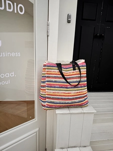 Detail of multi-color striped straw tote bag with black leather handles on a white stair