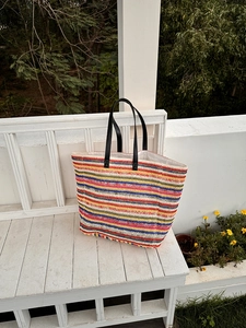 Detail of colorful striped woven tote bag with premium black leather handles outdoors