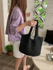 Detail of black woven tote bag featuring intricate hollow mesh and integrated handle