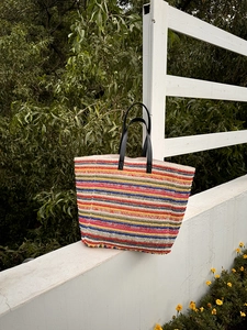 Detail of colorful striped woven tote bag featuring black leather handles and straw texture
