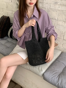Fashionable black woven straw tote bag held by a model in a casual lifestyle setting