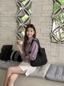 Detailed view of a hand-woven black straw tote bag paired with a casual summer outfit