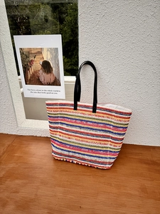 Close-up of vibrant multi-color striped woven texture and black leather handles of a tote bag