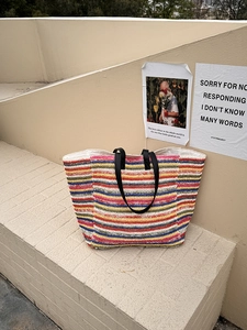 Close-up of a large multi-colored striped woven straw tote bag with black leather straps