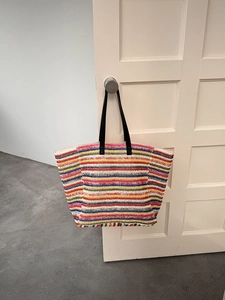 Detail of colorful striped woven straw tote bag hanging on a minimalist white door