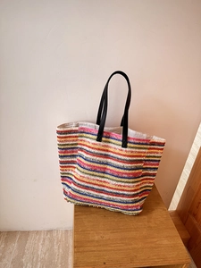 Detailed macro view of multi-color striped woven straw tote bag with black leather handles