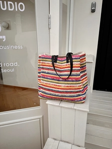 Detail of colorful striped woven straw tote bag with black leather shoulder straps