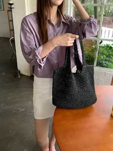 Close-up of a hand carrying a black woven straw tote bag in a bright lifestyle setting