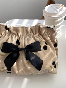 Detail of corduroy makeup bag with black cherry prints and a satin bow on a desk