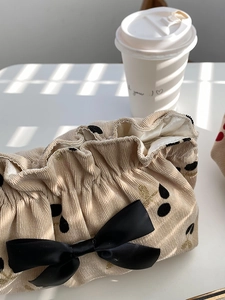 Detail of beige corduroy pouch featuring black cherry prints and a satin bow accent