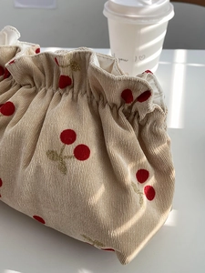 Detail of beige corduroy pouch featuring red cherry embroidery and elegant gold thread