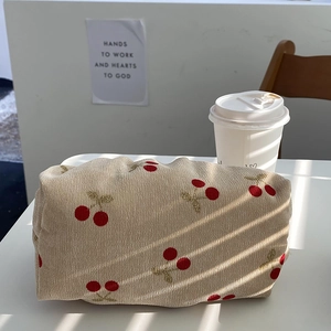 Detailed texture of beige corduroy cosmetic bag featuring red cherry embroidery pattern