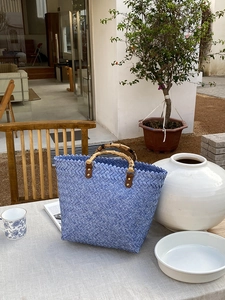 Detail einer blauen geflochtenen Tasche mit Bambusgriff und Textur auf einem Gartentisch