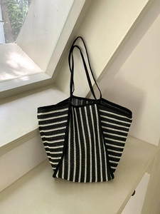 Detail of striped straw tote bag showing woven texture and black shoulder strap