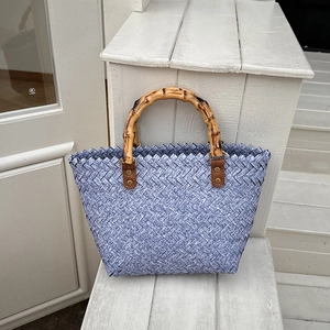 Detail of blue woven tote with natural bamboo handle and brown leather rivet connection