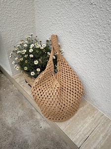 Detailed close-up of handmade hollow woven straw shoulder bag with natural mesh texture