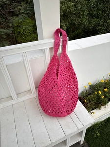 Detail of magenta crochet tote bag featuring intricate openwork weave on white wooden bench