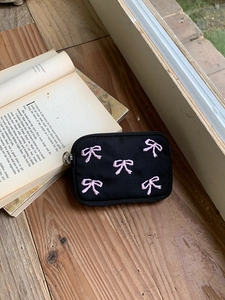 Detail of black canvas pouch with pink bow embroidery on a rustic wooden window sill