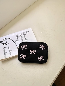 Close-up of black canvas coin purse with pink embroidered bows and metal zipper closure