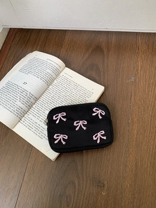 Close-up of pink bow embroidery on black canvas pouch over an open book background
