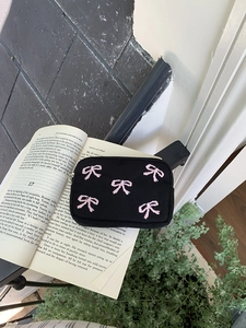 Detail shot of black canvas pouch with pink embroidered bows and secure zipper closure
