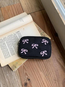 Close-up of black canvas pouch with pink 3D embroidered bows on a vintage book