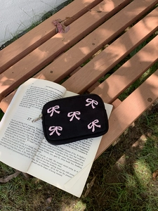 Detail of black canvas pouch with pink embroidered bows on a book in sunlight