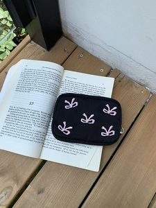 Close-up of black canvas pouch with pink embroidered bows on a vintage book backdrop