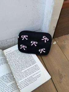 Sweet black storage pouch with pink embroidered bows, shown flat on an open book background