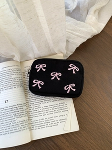 Detail shot of black canvas mini pouch with pink embroidered bows on a book background