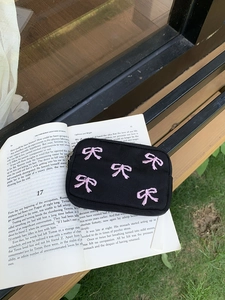 Cute black fabric coin purse with pink bow embroidery on an open book in nature