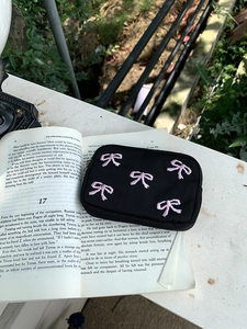 Macro shot of black pouch with pink embroidered bows on a vintage book background