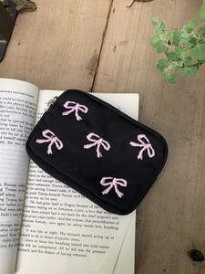 Close-up of black canvas storage bag with pink embroidered bows on vintage book and wood