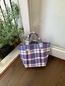 Detail of red, white and blue woven canvas tote bag with reinforced top handle on wood floor