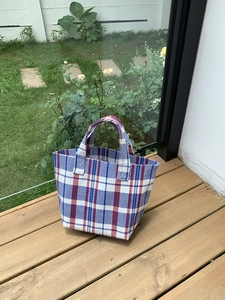Detail of red, white, and blue checkered woven tote bag placed on an outdoor wooden deck