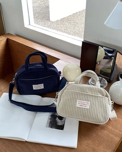 Detailed view of mini corduroy boston bags in navy and cream on a wooden desk