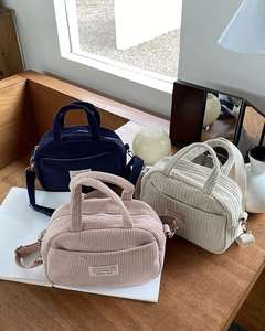 Three corduroy mini bowling bags in blue, pink, and beige on a wooden bench