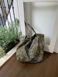 Detailed view of an olive green paisley canvas tote bag on a rustic wood floor