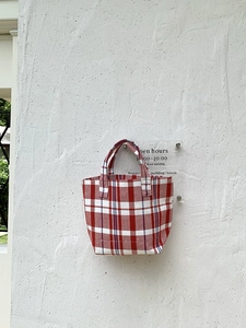 Detail of red and white checkered canvas tote bag with woven texture in a soft outdoor setting