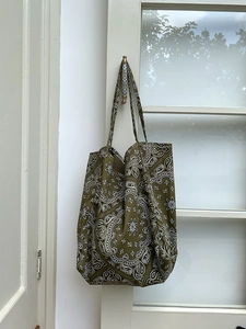 Olive green paisley canvas tote bag hanging on a handle in a minimalist bright setting