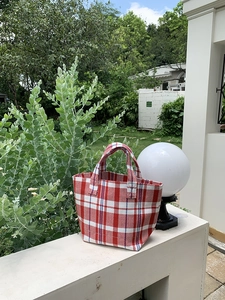 Detail shot of a red and white checkered canvas tote bag with woven texture on a stone stand