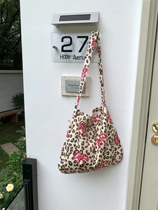 Detail of leopard print tote bag with pink bow pattern hanging on a white wall outdoors