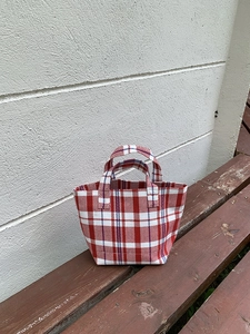 Detail of red and white checkered woven tote bag placed on a rustic wooden bench