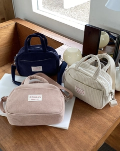 Three corduroy mini bowling bags in navy, pink, and beige stacked on wooden desk