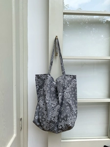 Detail of dark grey paisley canvas tote bag hanging on a door with soft natural lighting