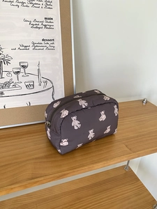 Close-up of quilted grey cosmetic bag with white bear pattern on a wooden shelf