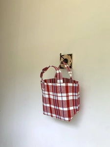 Detail of red and blue checkered woven tote bag hanging on a vintage wooden wall hook