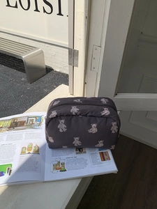Detail view of a large dark brown teddy bear print makeup bag on a magazine