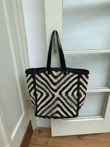 Detail of the woven tote bag featuring geometric patterns and black faux leather straps