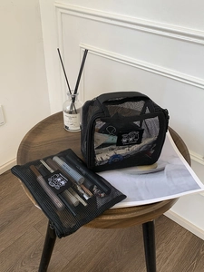 Detail of black mesh cosmetic bag set on a wooden stool with toiletries visible inside
